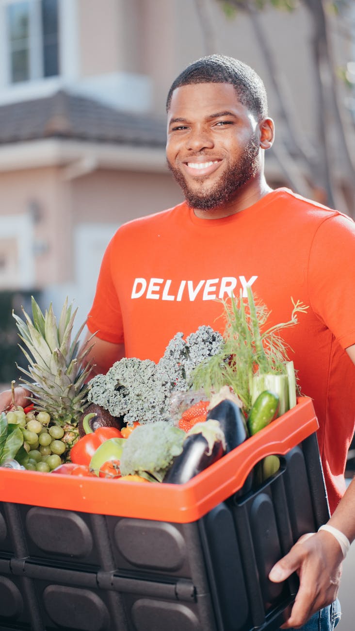 man in orange shirt holding black and orange plastic box with fresh vegetables